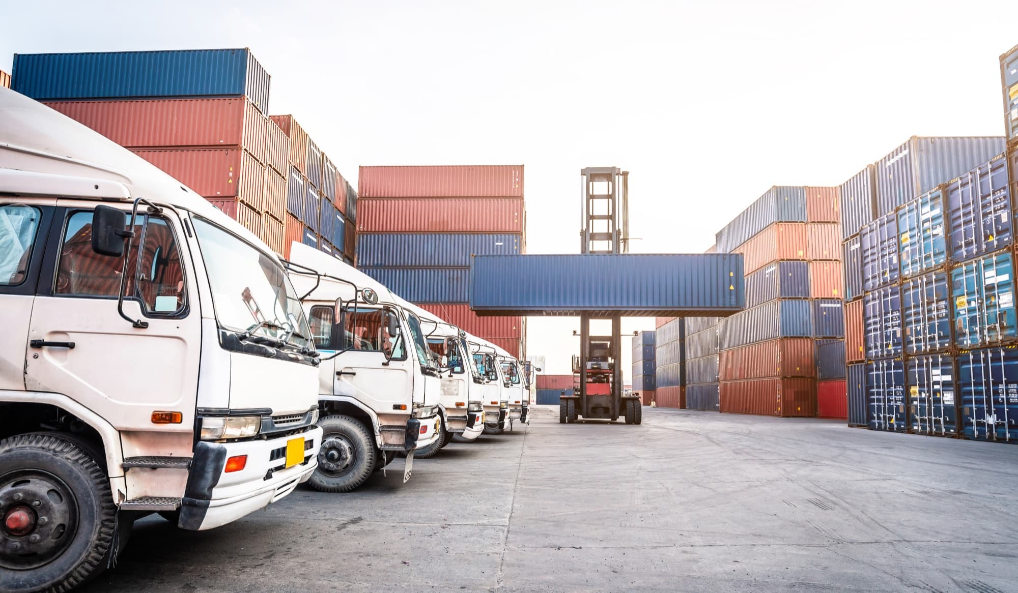 Logistics trucks parked beside shipping containers at a container yard for 3PL operations